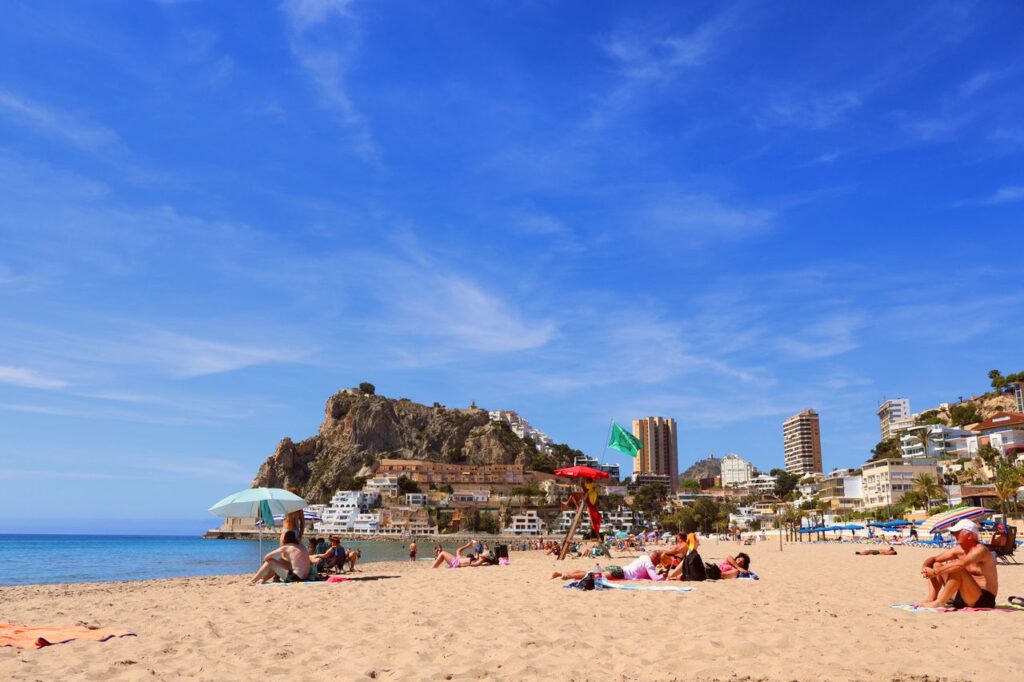 Golden sands of Postiguet Beach in Alicante with Santa Bárbara Castle rising above the Mediterranean coastline.